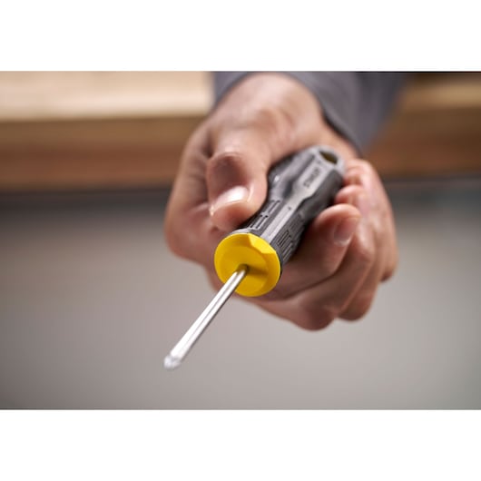 Hand holding a Stanley screwdriver with a yellow and black handle, pointed tip facing forward.