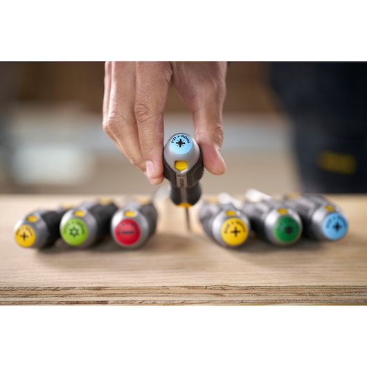 Hand picking a color-coded screwdriver from a set of STANLEY screwdrivers on a wooden surface.