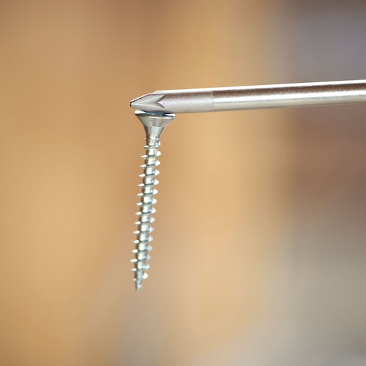 Close-up of a screwdriver bit holding a silver screw with blurred brown background.