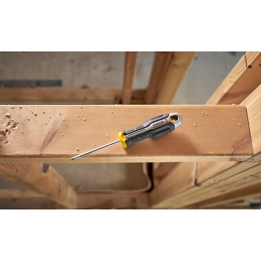 Stanley screwdriver with black and yellow handle lies on a wooden beam in a construction setting.