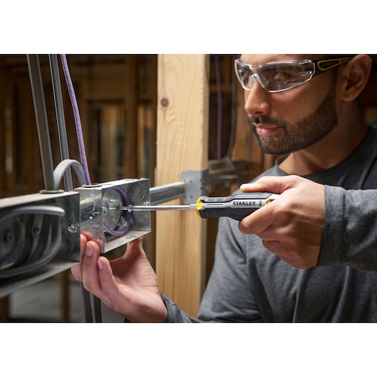 Person using a STANLEY screwdriver to fix wires in a metal electrical box on a wooden frame.