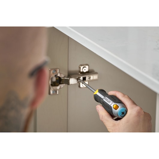 Person uses a STANLEY screwdriver to adjust a cabinet hinge under a countertop.