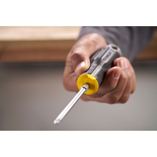 Hand holding a STANLEY screwdriver with a yellow and black handle, pointed towards the camera.
