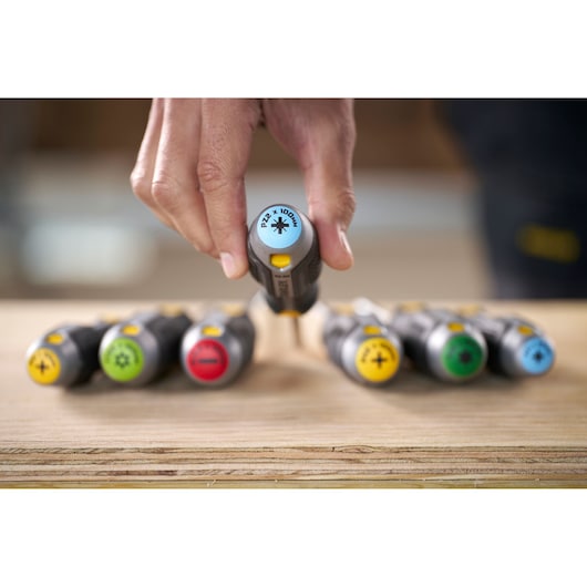 Hand picks a color-coded screwdriver from a row of STANLEY screwdrivers on a wooden surface.