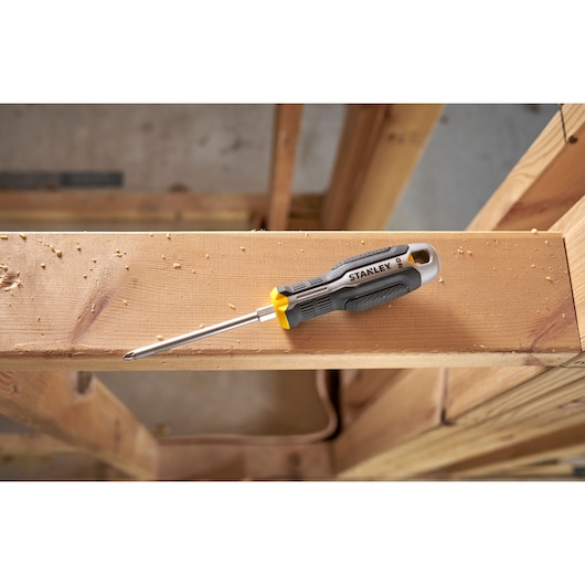 Stanley Phillips screwdriver with gray and yellow handle placed on a wooden beam at a construction site.