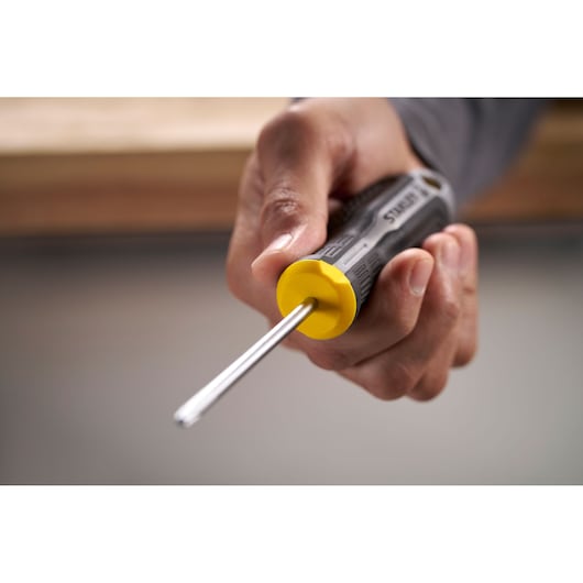 Hand holding a STANLEY screwdriver with a yellow and black handle, pointed tip facing forward.