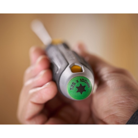 Hand holding a STANLEY T25 x 100mm screwdriver with a green end and ergonomic grip.