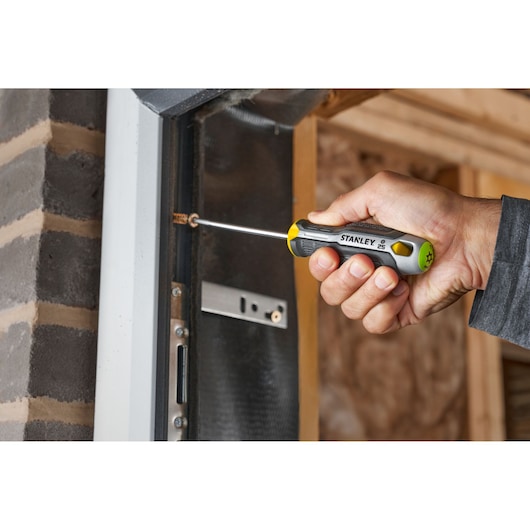 Hand using Stanley screwdriver to tighten screw on metal door frame.