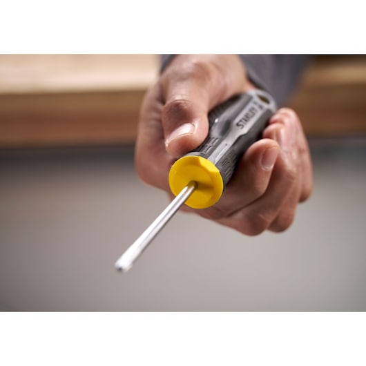 Close-up of a hand holding a Stanley screwdriver with yellow handle, pointing forward.