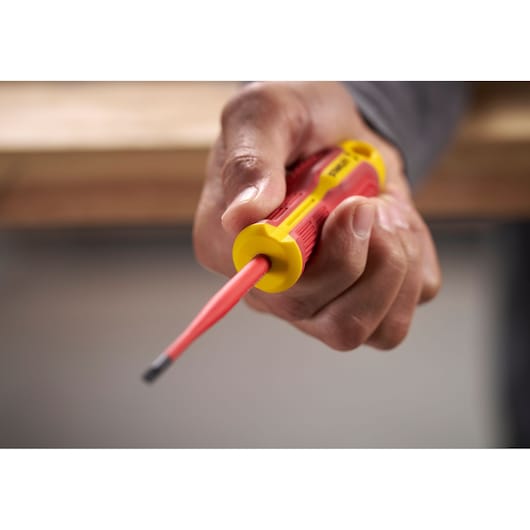 Hand holding a Stanley insulated screwdriver with red and yellow handle, pointed towards camera.