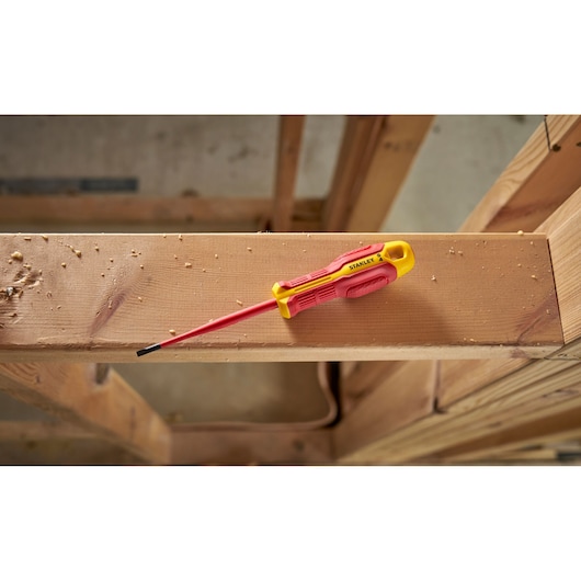 Stanley insulated screwdriver with red and yellow handle on a wooden beam in a workshop setting.