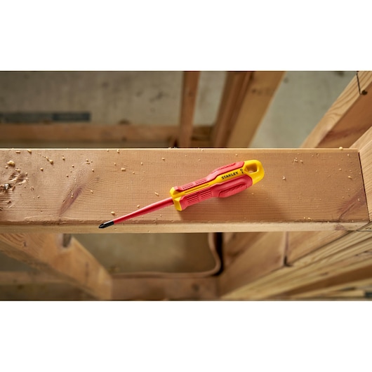 Stanley insulated screwdriver with red and yellow handle resting on a wooden beam in a construction setting.