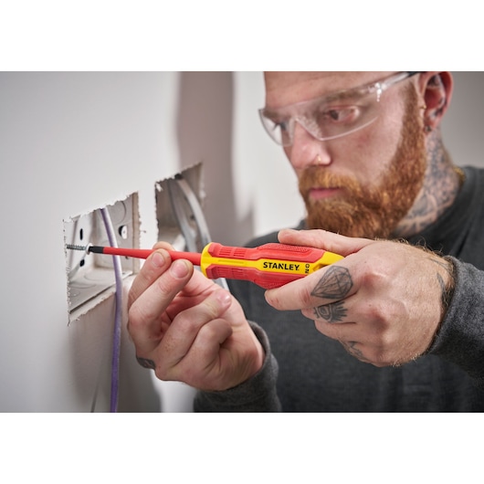 Person uses a Stanley insulated screwdriver to secure wires in an electrical socket on a wall.
