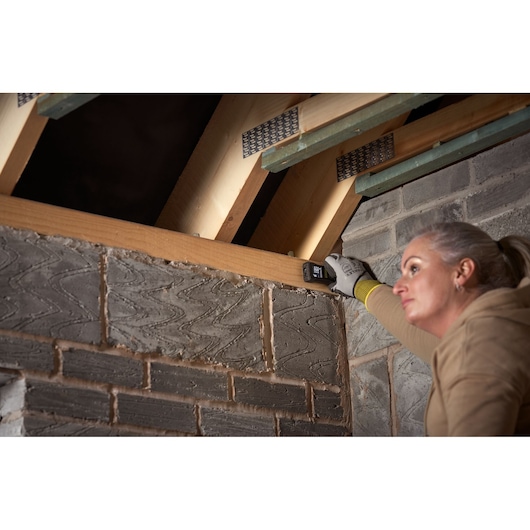 Photo of STANLEY FMHT77165-0 laser measurer held against wood beam in loft construction area.