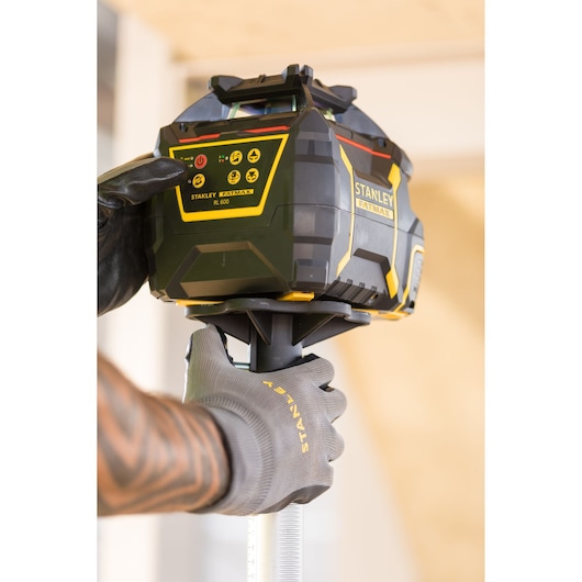 Photo of STANLEY FMHT77446-1 rotary laser level being operated by a gloved hand on a construction site.
