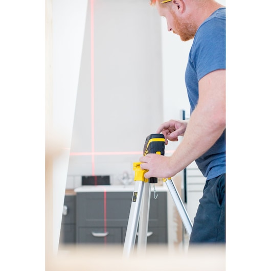 Photo of STANLEY FMHT77585-1 laser level on tripod, projecting red lines in interior workspace.