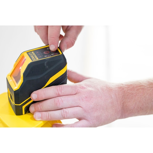STANLEY FMHT77585-1 laser level device in use, close-up of hand pressing control buttons.