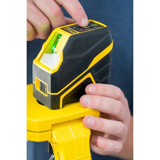 STANLEY FMHT77586-1 cross line laser level with green beam on tripod, close-up of hands operating top buttons.