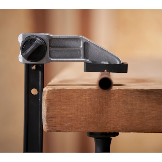 STANLEY FMHT83008-0 clamp mounted on wooden workbench, side angle, holding a metal pipe.