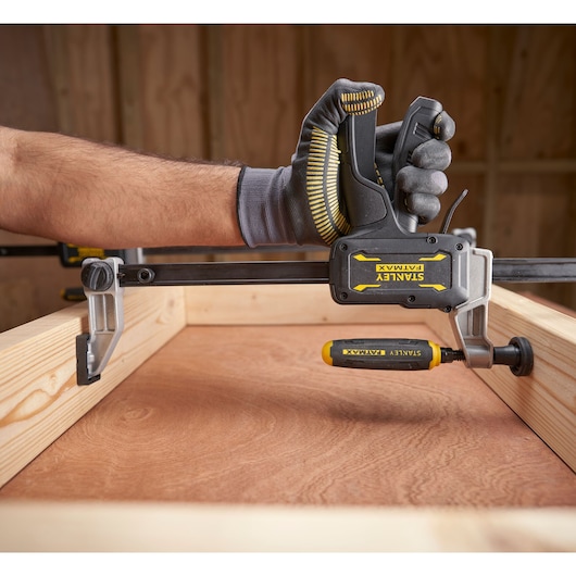 Photo of STANLEY FMHT83008-0 clamp being used to secure wooden boards, gloved hand operating the tool.