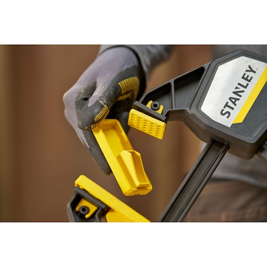 STANLEY FMHT83282-0 clamp held in gloved hand, close-up showing yellow jaw and black handle