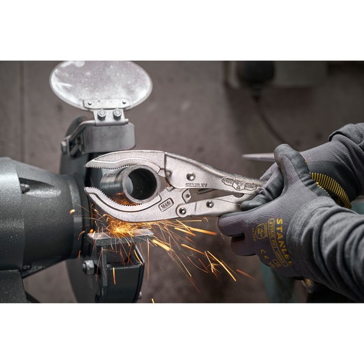 Stanley locking pliers gripping metal pipe as sparks fly from grinder in workshop.