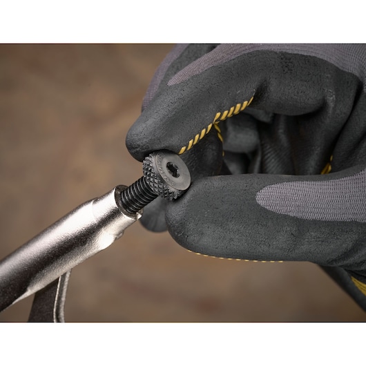 Gloved hand tightening a textured screw on a metal tool against a blurred background.