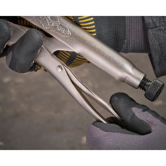 Gloved hands adjust a metallic locking plier with textured grip and adjustment screw, seen in close-up.