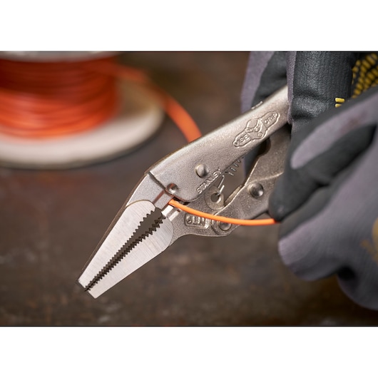 Gloved hand using STANLEY locking pliers to grip an orange wire with spool in the background.