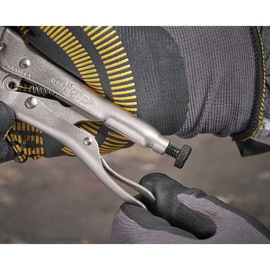 Stanley locking pliers being adjusted by gloved hands on a work surface.