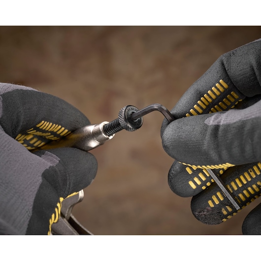 Gloved hands using an Allen key to adjust a screw on a Stanley tool against a blurred background.