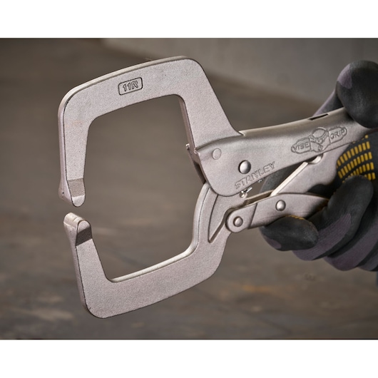 Metal C-clamp locking pliers held in a gloved hand, used for gripping and clamping workpieces securely.