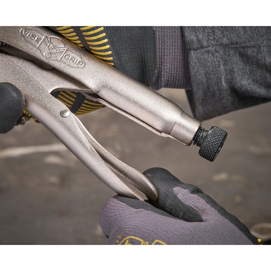 Gloved hands adjust a locking plier tool with a textured screw knob in a workshop setting.