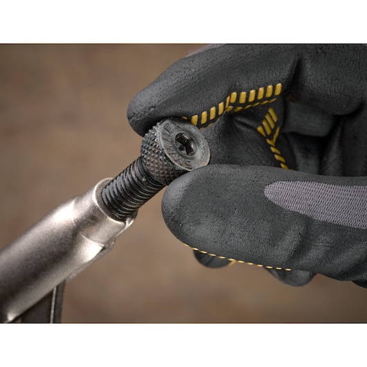 Gloved hand holding a textured screw attached to a metal tool, close-up view.