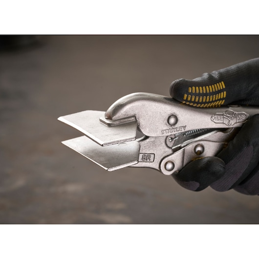 Stanley metal locking pliers holding two flat metal plates, shown in a gloved hand, close-up view.