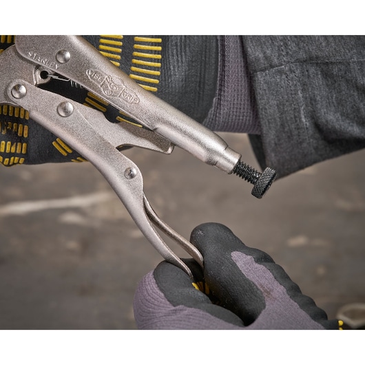 Stanley locking pliers held by gloved hands, adjusting the clamp screw, close-up on tool and gloves.