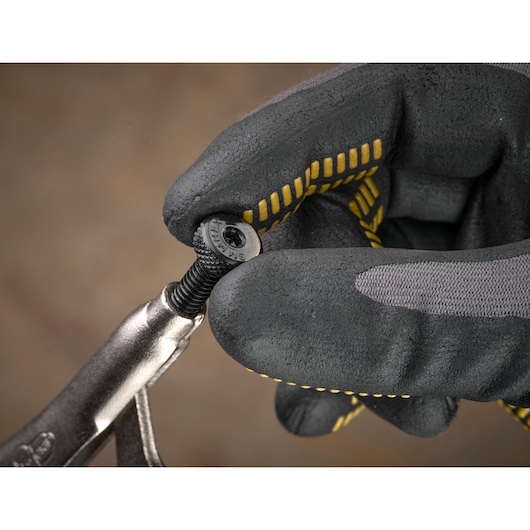 Gloved hand holds a screw and locking pliers close-up. Tool and screw details are visible.