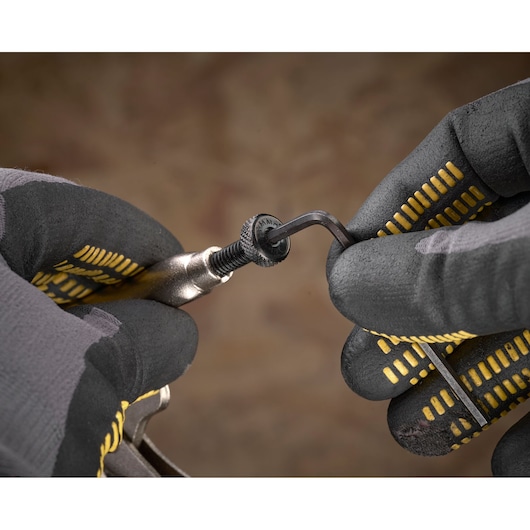 Gloved hands use an Allen key to tighten a bolt on a metal tool against a blurred background.