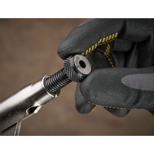 Gloved hand adjusting a metal tool screw with textured grip, branded STANLEY, against a blurred background.