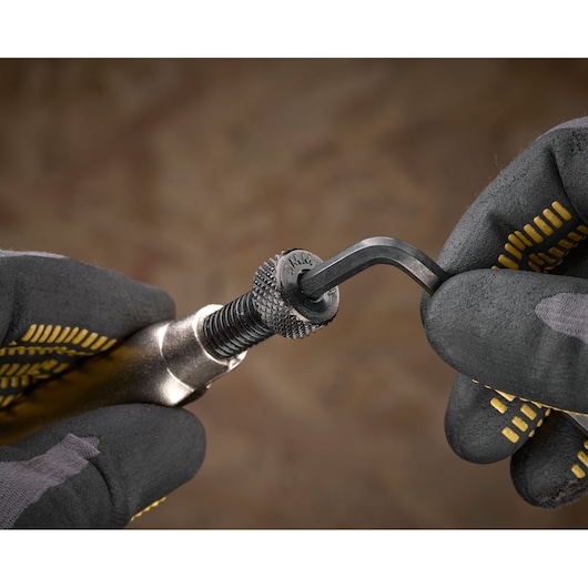 Gloved hands adjust a metallic tool with a hex key. Close-up, textured grip visible. STANLEY branding on tool.