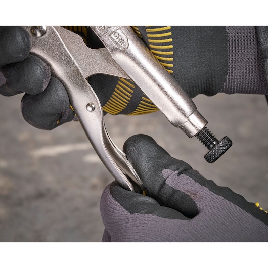 Gloved hands adjusting a metallic locking plier on a workshop surface.
