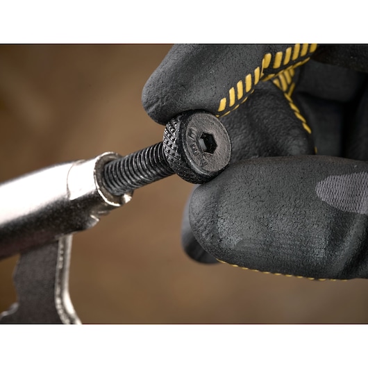 Gloved hand holding a black hex screw with textured head using a metal tool, close-up view.