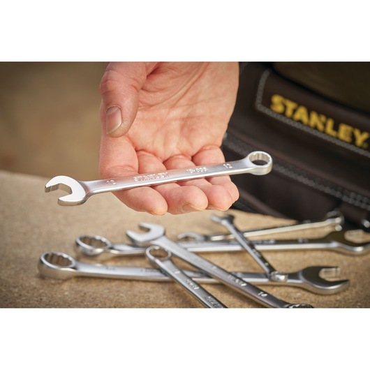 STANLEY FMMT13035-0 spanner held in hand, with other wrenches on a workbench, close-up angle.