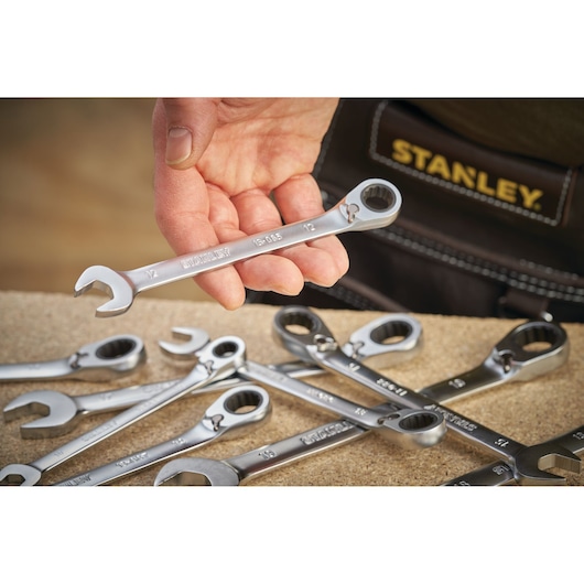 STANLEY FMMT13084-0 ratcheting wrench held in hand, with several wrenches on workbench, photography close-up.