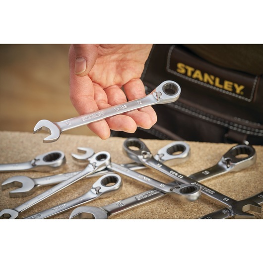 Stanley FMMT13094-0 ratcheting spanner held in hand, with other wrenches on work surface, close-up angle.