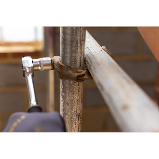 STANLEY FMMT17228-0 ratchet wrench tightening scaffold clamp, close-up in industrial setting.