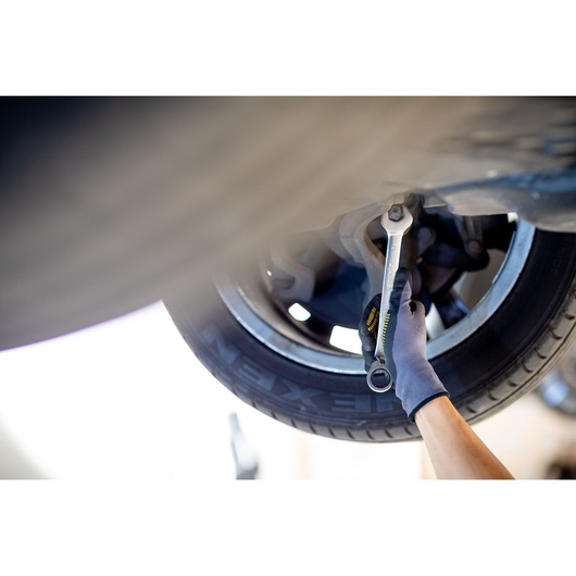 STANLEY FMMT82849-0 ratcheting wrench tightening bolt on car suspension, gloved hand visible, close-up.