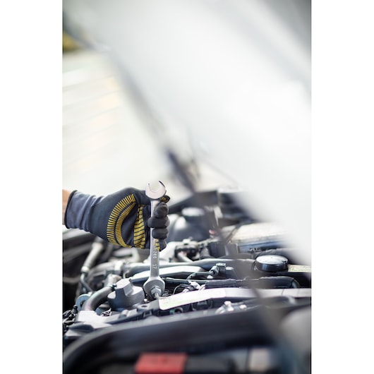 STANLEY FMMT82901-0 wrench in gloved hand tightening bolt in car engine bay, side angle, photography.