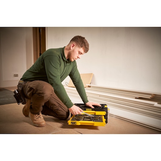 STANLEY FMMT98107-1 tool set in yellow box on floor, opened by kneeling worker in construction setting.
