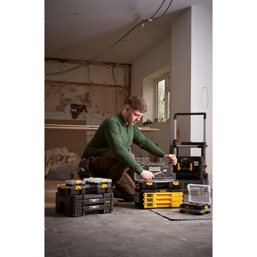 Person organizing STANLEY toolboxes and containers in a room under renovation. Various tool storage units are visible.